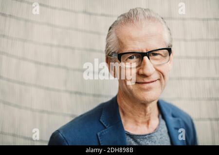 Portrait of confident senior businessman wearing glasses against wall Stock Photo