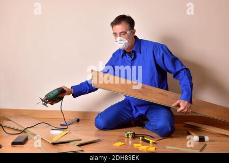 Professional parquet assembler with cutting machine in hand sitting on the floor assembling parquet. Horizontal composition. Stock Photo
