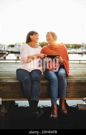Full length of happy senior women using digital tablet on pier Stock Photo
