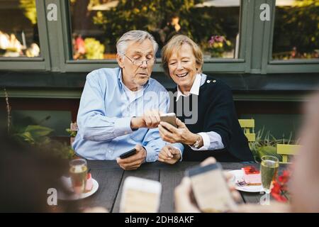 Happy senior couple using mobile phone at outdoor restaurant Stock Photo