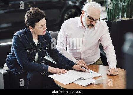 Senior man and woman analyzing documents while sitting at car showroom Stock Photo