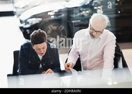 Senior man and woman reading documents while sitting at car showroom Stock Photo