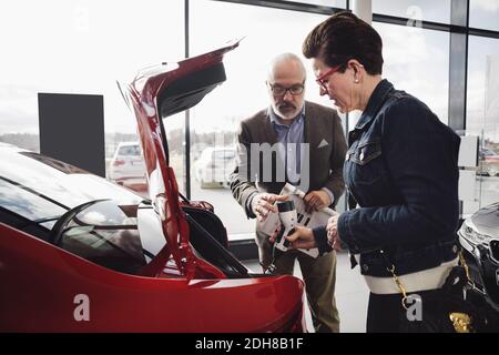 Senior man and woman examining charger of electric car at showroom Stock Photo