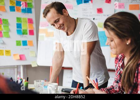 Smiling businessman standing by female colleague working on table Stock Photo