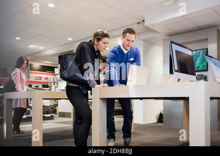 Salesman assisting female customer in buying laptop at store Stock Photo