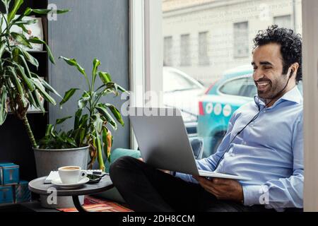 Happy businessman using laptop while sitting by window in creative office Stock Photo