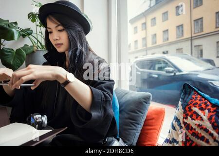 Young female blogger photographing through smart phone while sitting by window in office Stock Photo