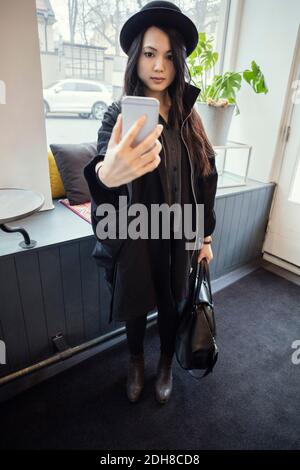 Full length of young businesswoman taking selfie while standing in modern office Stock Photo