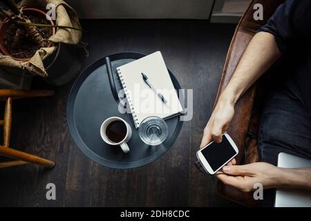 Cropped image of businessman using phone while sitting by drinks and spiral notebook Stock Photo