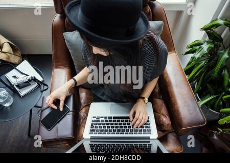 High angle view of female blogger using phone and laptop while sitting on chair Stock Photo