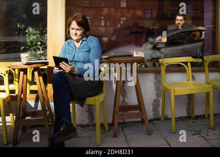 Female owner using digital tablet while sitting at sidewalk cafe Stock Photo