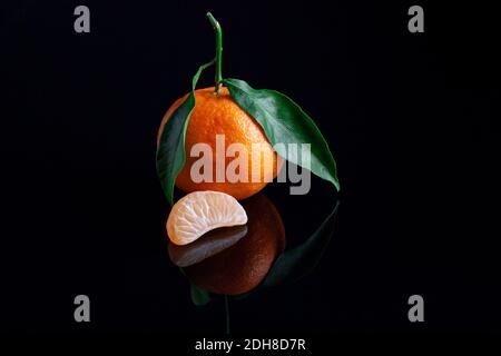 Delicious and beautiful Tangerines with green leaf. Peeled Mandarine orange and Tangerine orange slices on a Dark reflective surface. Stock Photo