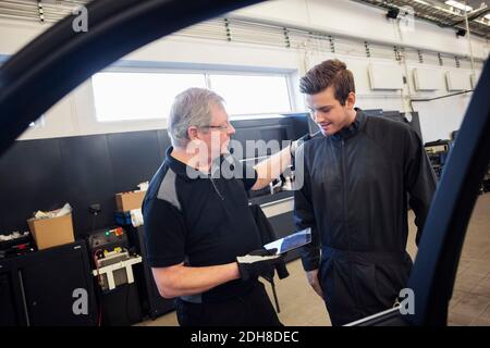 Mechanics using digital tablet seen through car window at auto repair shop Stock Photo