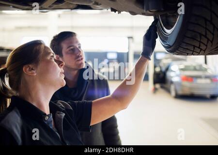 Close-up of mechanic showing wheel to customer under car at repair shop Stock Photo