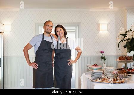 Portrait of smiling owners standing by dessert decorated table at cafe Stock Photo