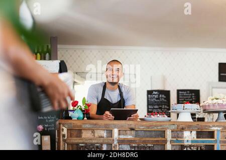 Smiling baker holding digital tablet while looking at female colleague in cafe Stock Photo