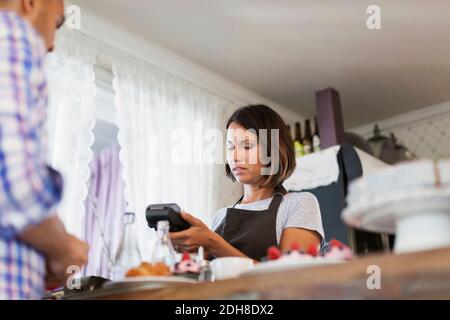 Serious baker using credit card reader while man standing at cafe counter Stock Photo