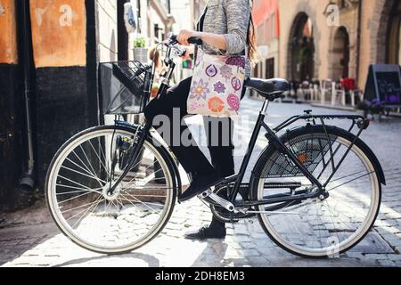 Low section of woman standing with bicycle on cobbled street Stock Photo