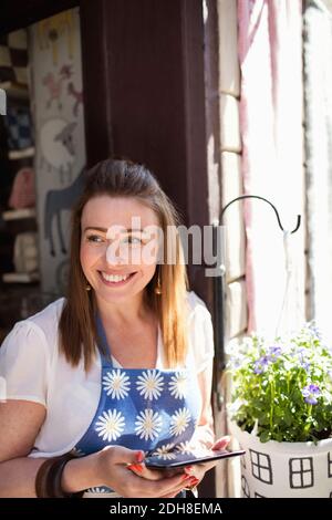 Happy female owner using digital tablet while standing at entrance of fabric shop Stock Photo