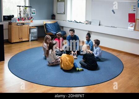 Teacher playing with students while sitting on floor at school Stock Photo