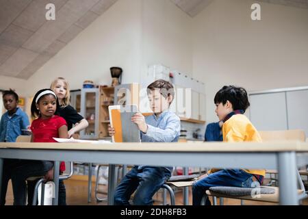 Students looking at boy using digital tablet in classroom at school Stock Photo