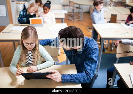 High angle view of teacher assisting female student while using digital tablet in classroom Stock Photo