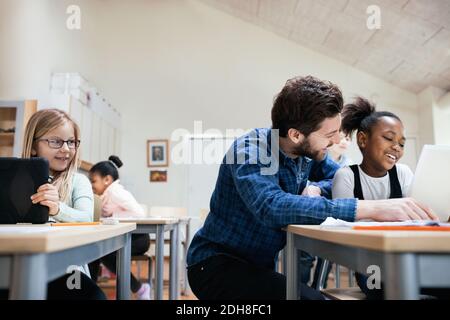 Smiling teacher with students using digital tablet at classroom Stock Photo