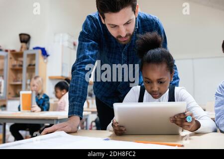 Teacher looking at girl using digital tablet in classroom Stock Photo
