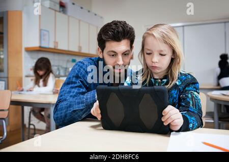 Male teacher explaining student in using digital tablet at classroom Stock Photo