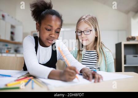 Girl assisting friend while studying in classroom at school Stock Photo