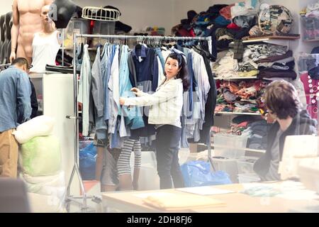 Woman talking to volunteer while searching for clothes in rack at workshop Stock Photo
