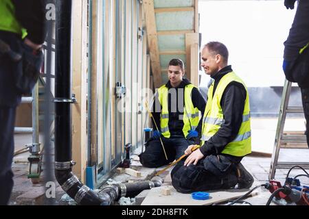 Thoughtful manual workers looking at pipe while working in construction site Stock Photo