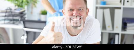 Happy man lie on couch and show her hand class. Stock Photo