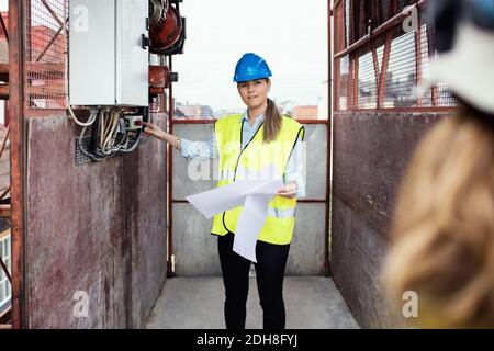 Construction manager holding documents while showing machinery in construction elevator Stock Photo