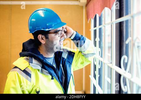 Construction worker talking on phone while standing by window in industry Stock Photo