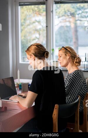 Mother and son using laptop at dining table by window Stock Photo