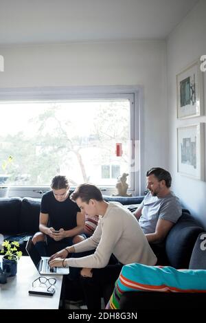 Men using technologies while sitting with father in living room Stock Photo