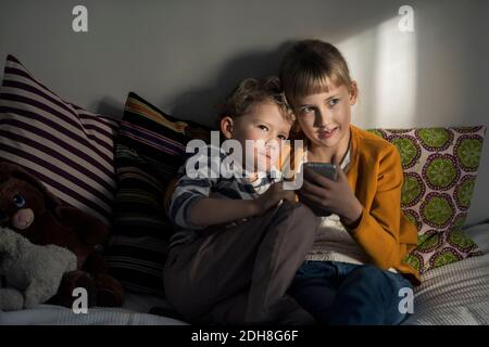 Siblings using mobile phone while sitting on sofa at home Stock Photo