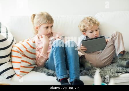 Siblings using digital tablet and mobile phone at home Stock Photo