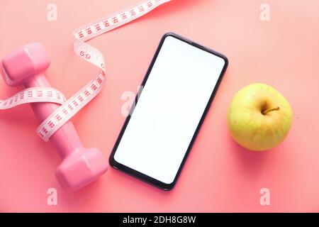 healthy diet concept with smart phone, apple and dumbbell on pink background  Stock Photo