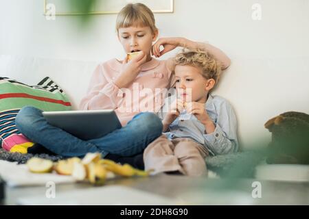 Siblings using digital tablet while eating apples at home Stock Photo