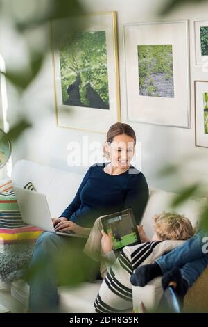 Happy mother looking at boy using digital tablet Stock Photo