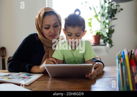 Mother assisting son in using digital tablet while studying at home Stock Photo