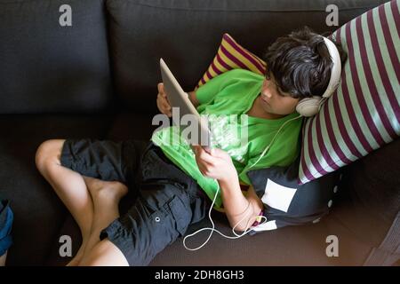 High angle view of boy listening music through digital tablet while reclining on sofa at home Stock Photo