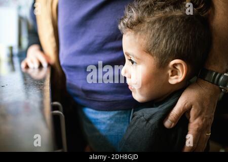 Thoughtful boy looking away while standing by father in kitchen Stock Photo
