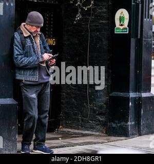 Kingston London, December 09 2020, Middle Aged Man Standing In A Pub Doorway Using His Mobile Phone Or smartphone Stock Photo