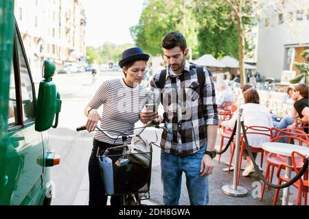 Couple using smart phone while standing by sidewalk cafe Stock Photo