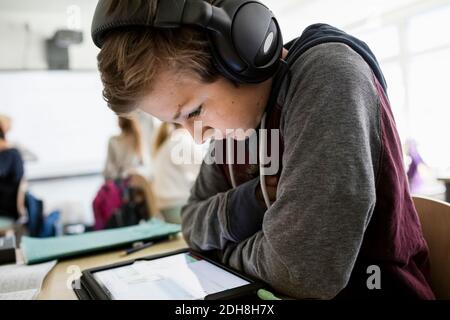 Side view of boy listening to headphones while using digital tablet in classroom Stock Photo