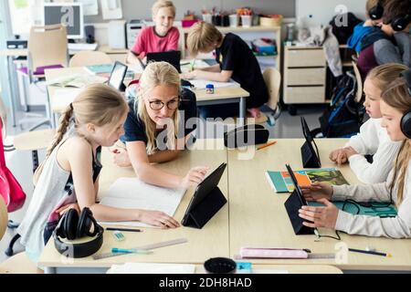 Teacher assisting high school girl using digital tablet in classroom Stock Photo