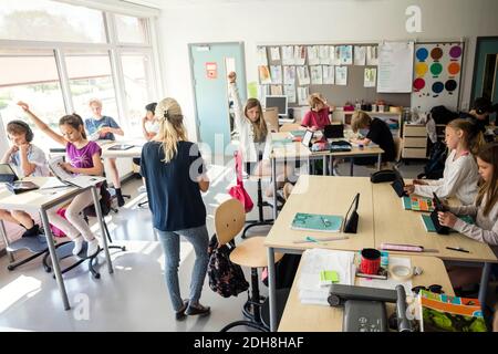 High school students raising hands with teacher in classroom Stock Photo